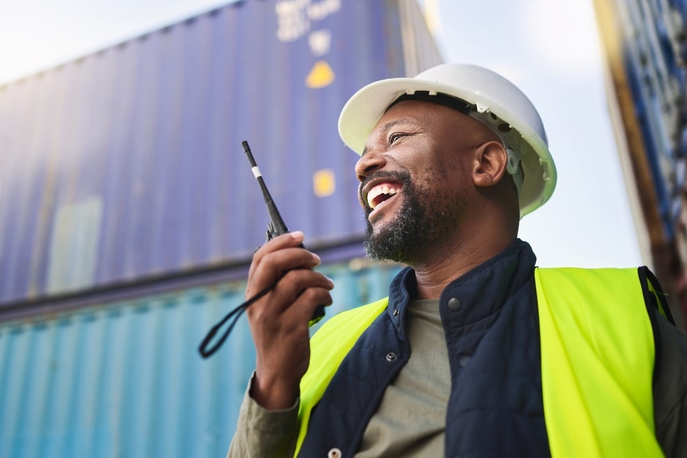 Man smiling using a radio with cargo containers in the background